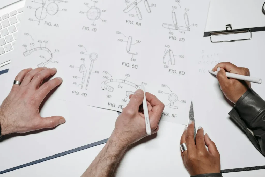 Tim desainer produk sedang berdiskusi dan membuat sketsa di atas meja kerja dengan berbagai alat desain
